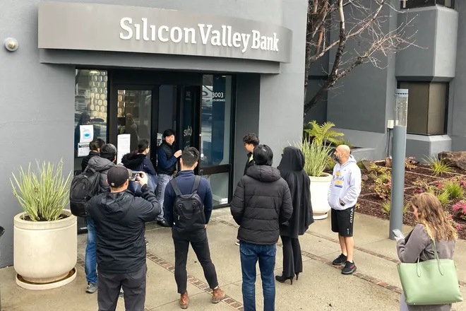 A person from inside Silicon Valley Bank, middle rear, talks to people waiting outside of an entrance to Silicon Valley Bank in Santa Clara, Calif., on March 10, 2023. The failure of SVB and Signature Bank, the second and third largest bank failures in U.S. history, heightened investor concern about the health of our banking industry. (Jeff Chiu, AP)