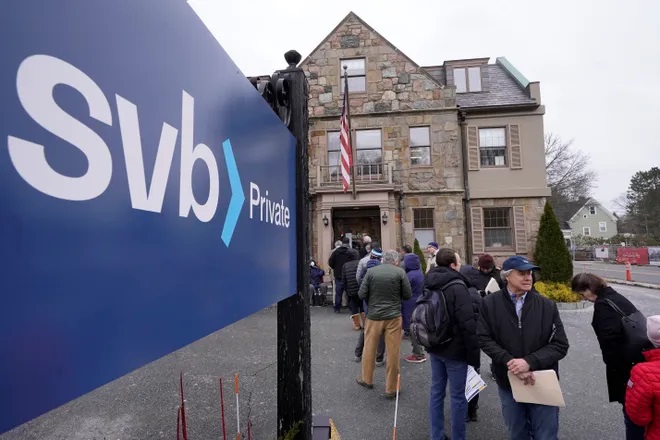Customers and bystanders form a line outside a Silicon Valley Bank branch location, Monday, March 13, 2023, in Wellesley, Mass. The sudden crisis in the U.S. banking industry is sure to cause some tightening of lending and credit and a slowdown in the pace of borrowing and spending. (credit: Steven Senne, AP)